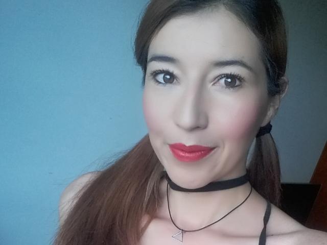 AntonnellaS has brown pigtails, red lipstick, black choker, and a necklace with a triangular pendant. She's smiling with pink cheeks and dark eyeliner.