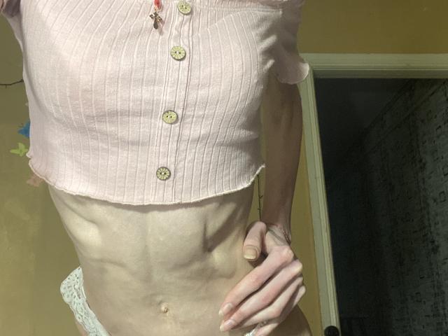 Kabblasha's skinny, pale torso with visible ribs, wearing a pink ribbed button-up shirt, exposing a flat, muscular belly and white lace underwear. Hand on hip.