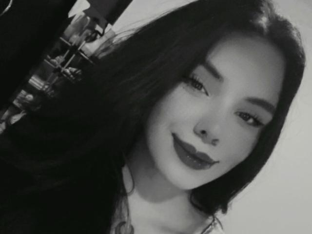 Fotografia in bianco e nero di GuadalupeClak con lunghi capelli scuri, labbra piene e eyeliner, che sorride leggermente. Indossa un rossetto scuro e un piercing al naso. Il suo seno non è visibile..