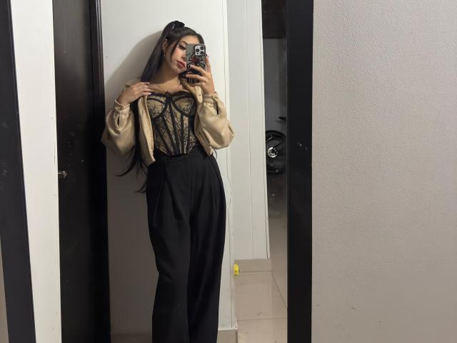 MilenaRossi with long dark hair, wearing a beige lace top, black high-waisted pants, and a black jacket, taking a mirror selfie, showing her tits and ass.