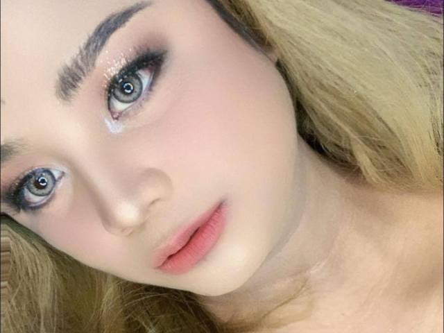 AlluringJhana heeft blauwe ogen, volle, roze lippen en blond haar met een lichte glans. Haar make-up omvat donkere eyeliner en een subtiele gloed op haar lichte huid..
