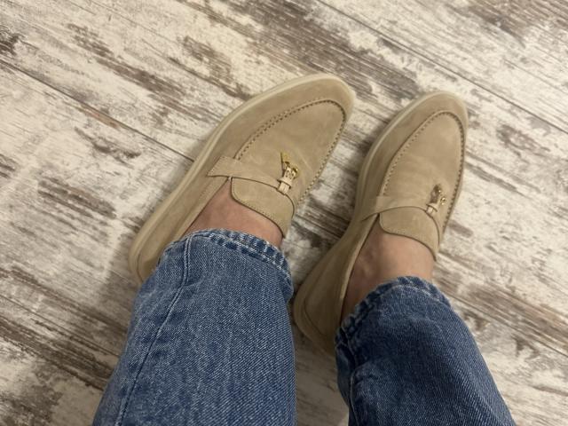Raichell's legs in blue denim jeans, wearing tan suede loafers with gold buttons, standing on a wooden floor.