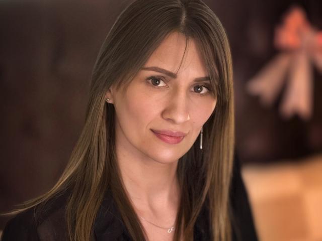 ChristyBrooks has long brown hair, subtle makeup, small earrings, and a slight smile. She's wearing a black top with a thin necklace, looking calm and attractive.
