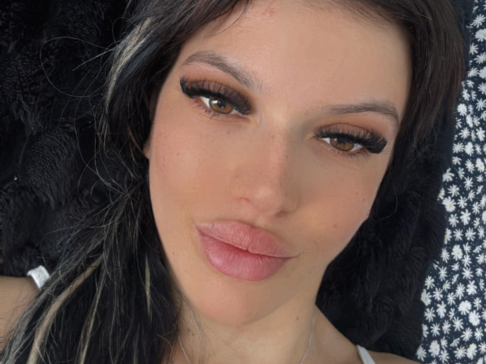 AndreeaG has brown eyes with thick, long eyelashes, pale pink lipstick, and black hair with blonde streaks. She's looking at the camera with a slight, pouty smile.