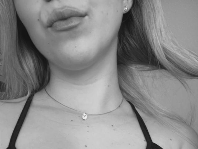 SugarrX's face, showing pouty lips, small earrings, and a necklace with a tiny gem. She's wearing a black halter top, exposing her neck and upper chest.