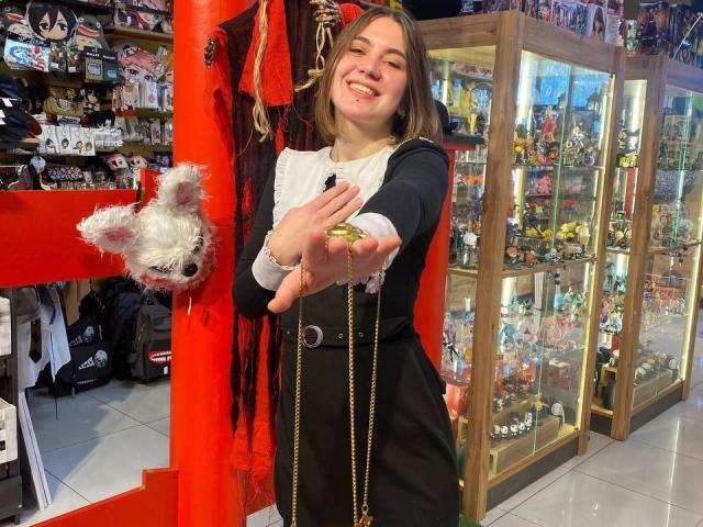 IsleBelle, smiling, holding a fluffy white toy dog, wearing a black dress with white chest, extends hand with gold ring, standing in a toy store.