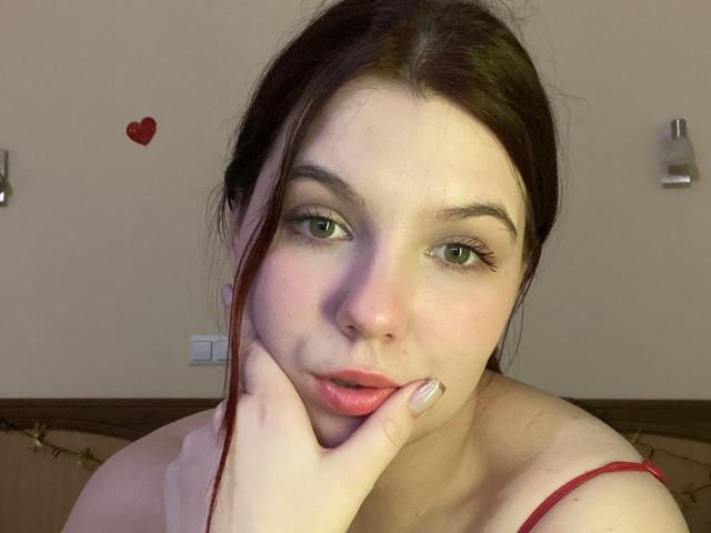 Khaleessi with pale skin, green eyes, and dark brown hair, pouting with red lipstick, hand on cheek, wearing red strap, looking at camera, slight blush, cute.