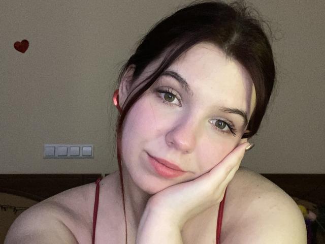 Khaleessi with pale skin, brown eyes, and dark hair, resting her head on her hand, wearing a red strap, has a small red heart sticker on the wall.