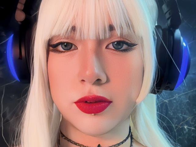 SabriPrettty with white hair, blue eyes, and red lipstick, wearing black headphones with blue lights, has a serious expression and a slight drop of saliva on her lower lip.