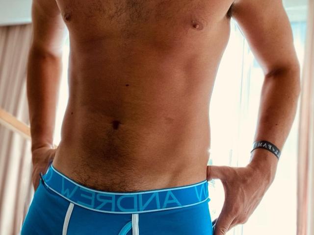 Rocko27's toned, tan-skinned torso, wearing tight blue underwear with a white waistband, hands on hips, a black wristband on the right wrist. Visible abs, slight chest hair.