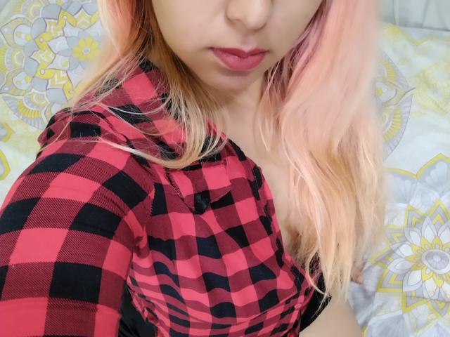 DulceFantasticoS with pink hair, red and black checkered shirt, and red lips, showing a bit of her tits. Her face is partially visible, with a soft, seductive look.
