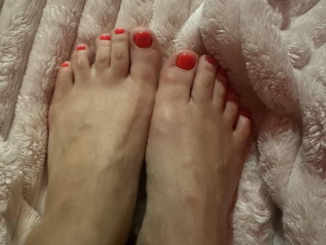 Les pieds de Stefanni, avec ses ongles de pieds peints en rouge, reposent sur une couverture rose et moelleuse. Sa peau est claire, et ses orteils sont légèrement recourbés..
