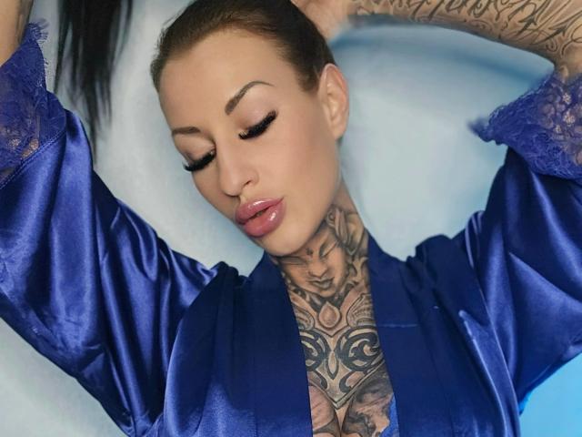 MeganSteel-hot with tattoos, blue satin robe, glossy pink lips, arms raised, long black hair, heavy eyeliner, and a sexy, confident look. Her tits are partially visible.