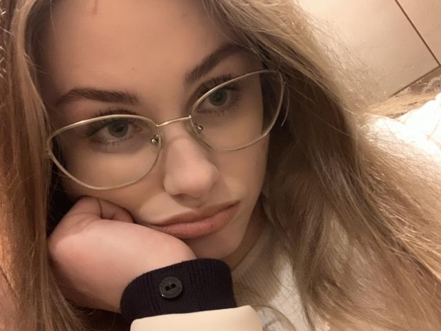 Isabel Lips, met een bril, leunt haar hoofd op haar hand, heeft bleke huid, groene ogen en blond haar, draagt een zwarte blouse met knoopjes en heeft een serieuze blik..