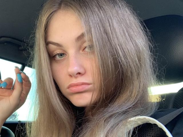 Isabel Lips, con lunghi capelli biondi, che fa l'occhiolino, occhi verdi e smalto blu, che appare seria in un'auto, indossa una giacca nera e bianca, mostrando il suo viso carino..