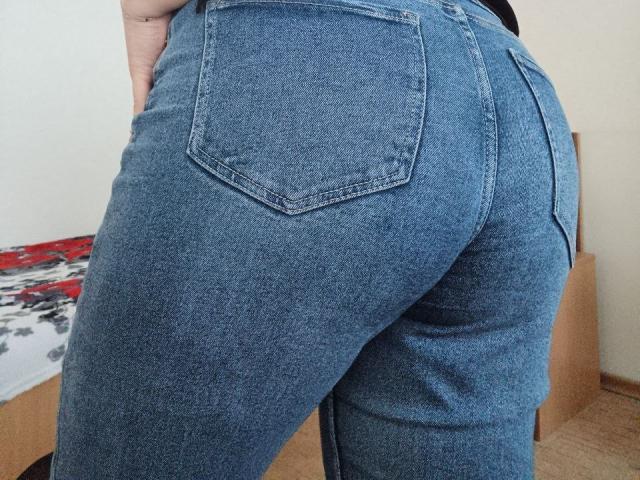 Leiliia's blue denim ass is prominent in the image, with her tight jeans highlighting her butt. Her back pockets are visible, and she's standing with her hand on her hip.