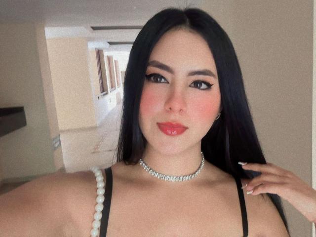 EimmyPark with long black hair, red lipstick, and a diamond choker, showing off her boobs in a black top. She's smiling with pink cheeks, looking at the camera.