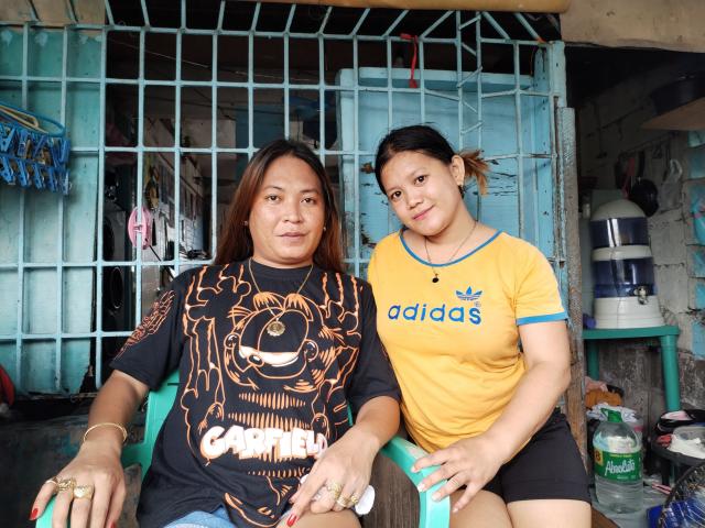 Two EXOTICPINAY women, one with brown hair and black shirt, the other with black hair and yellow Adidas shirt, sitting on green chairs, smiling at the camera.