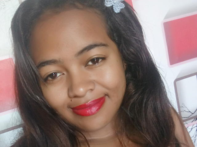 CiciahBella has brown skin, red lipstick, and dark wavy hair with a sparkly hair clip. She's smiling with a nose ring and brown eyes.