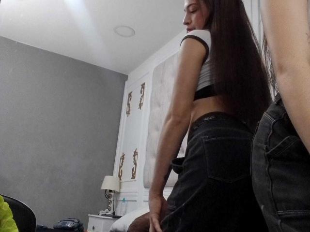 MadisonAngel, con lunghi capelli castani, un top bianco e una gonna nera, è in piedi con la schiena rivolta verso la telecamera, mostrando il suo sedere scoperto, accanto a un uomo con i jeans..