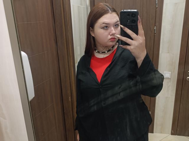 ArielXxl with red shirt, black shawl, choker, holding phone, mirror selfie, brown wood door, beige tiles, looking annoyed, brown hair, slight pout, medium tits, average build.