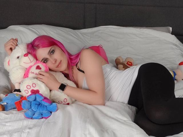 NeleSweet-hot with pink hair, white tank top, black tights, lying on bed, hugging white teddy bear, surrounded by stuffed animals, wearing black wristwatch, looking at camera.
