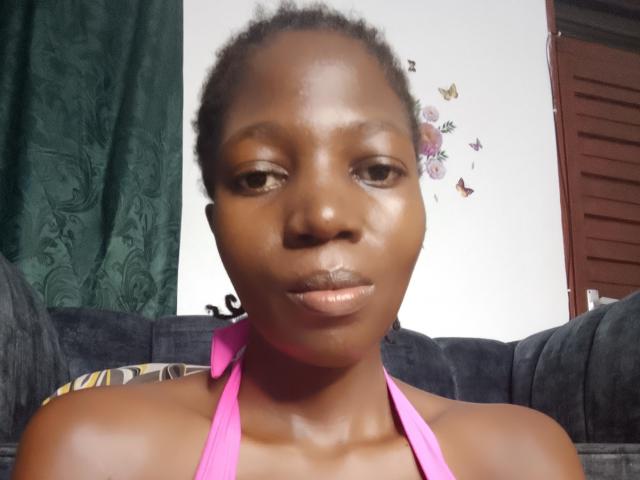 SexyWaist has dark brown skin, curly hair, and is wearing a pink halter top. She's looking at the camera with a neutral expression, and her lips are slightly parted.