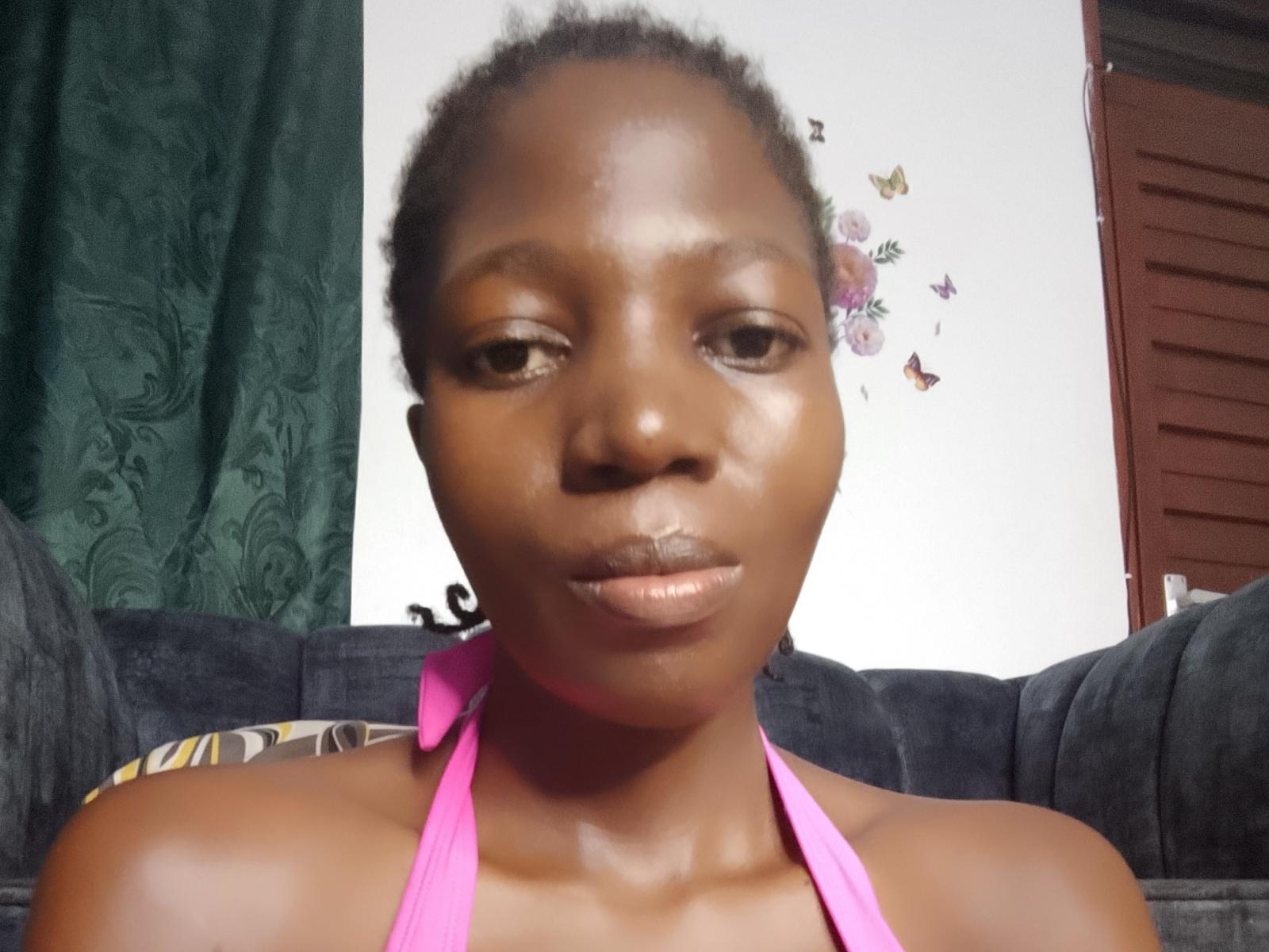 SexyWaist has dark brown skin, curly hair, and is wearing a pink halter top. She's looking at the camera with a neutral expression, and her lips are slightly parted.