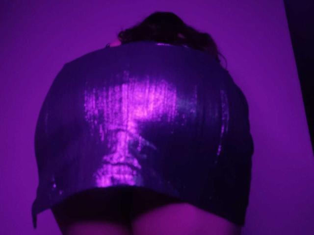 JackyEmma's shiny purple butt, wearing a tight, metallic mini-skirt, with her back to the camera, under purple lighting, showing her round, reflective butt cheeks.