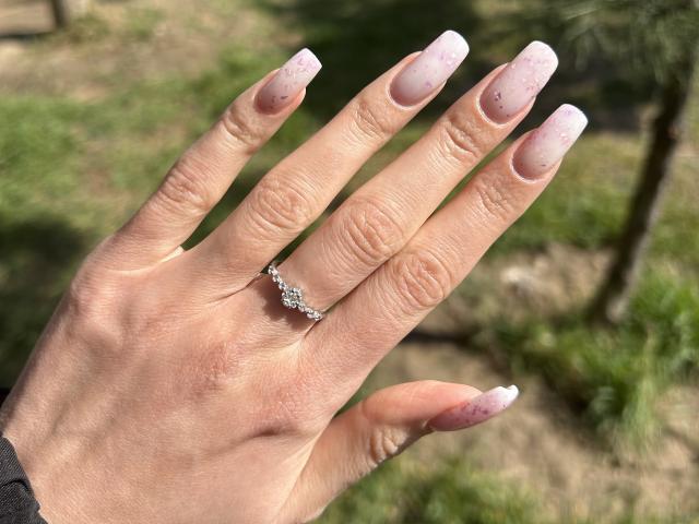 Karish's hand with long, pink-tinted, French-tipped nails, a diamond ring on the middle finger, and a slight tan. Her fingers are slightly spread, showing off the ring.