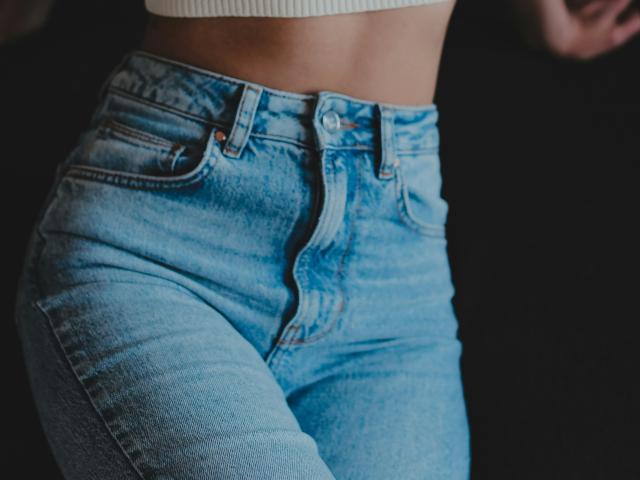 ImSweety's tight, blue, high-waisted jeans, showing their ass, with visible buttons and a white ribbed crop top, against a dark background.