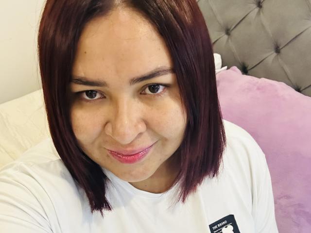 KarlaWild a une peau marron clair, des cheveux raides brun-roux, un petit nez et des lèvres roses, et elle porte une chemise blanche, avec une expression mignonne et légèrement plissée..