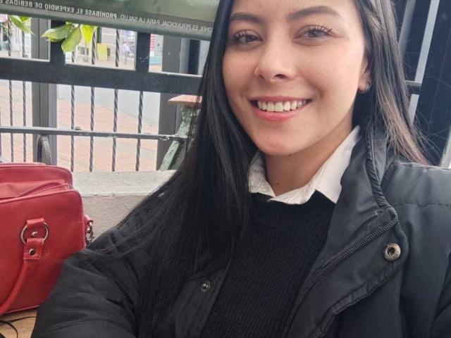 SophiaRamirez has long black hair, brown eyes, and a big smile with pink lipstick. She's wearing a black jacket over a white shirt and a red purse.