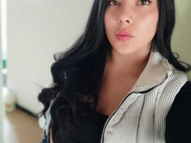 SophiaRamirez with long black hair, pouty pink lips, wearing a white ribbed vest over a black top, brown eyes, soft skin, looking directly at the camera.