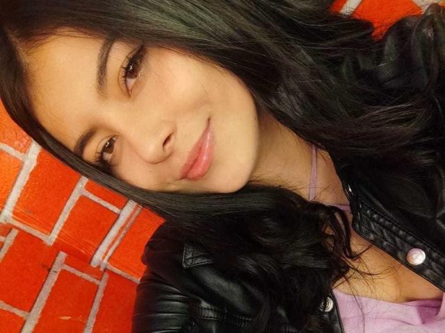 SophiaRamirez has long black hair, brown eyes, and a slight smile. She's wearing a black leather jacket over a pink top, showing a bit of cleavage.