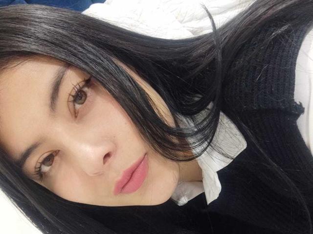 SophiaRamirez has long black hair, brown eyes, pink lips, and a cute face. She's wearing a black sweater over a white shirt. Her nose is slightly upturned.
