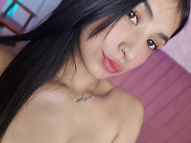NaiaSanders has long black hair, brown eyes, pink lips, a nose ring, and a zebra necklace. She's topless with shiny skin. Her ass is not visible.