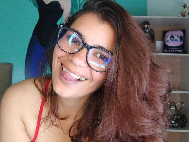 BulmaHot with glasses, tongue out, smiling, red bra, brown wavy hair, light skin, cute, sexy, attractive, happy, looking at camera.