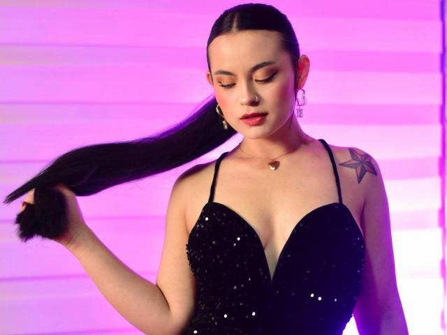 Ariana Rossy, vêtue d'une robe noire pailletée, avec une longue queue de cheval noire, un tatouage d'étoile sur l'épaule droite, un éclairage rose-violet, du rouge à lèvres rouge, un collier en or et des boucles d'oreilles créoles. Seins, mignonne, sexy..