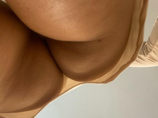 JazminSweet69 with medium brown skin, black wavy hair, red halter top showing her tits, holding phone in mirror, beige panties, wooden door in background.