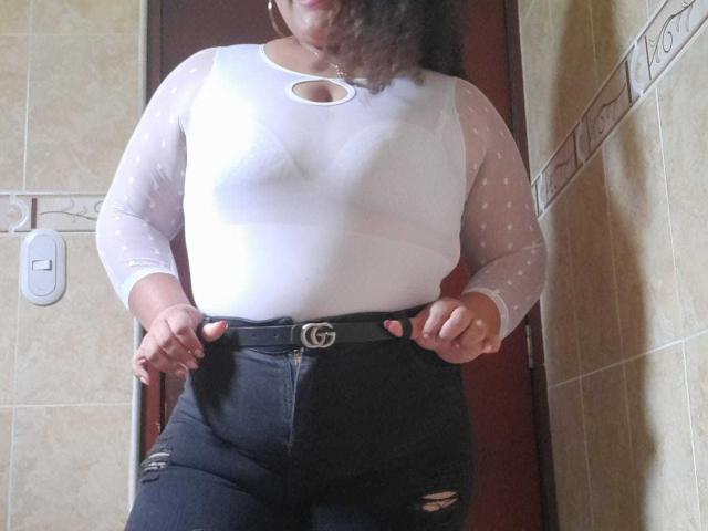 MelannieCarter wearing a white, semi-transparent, polka-dot long-sleeve top, showing her tits through the fabric, and black, high-waisted, ripped jeans with a Gucci belt.