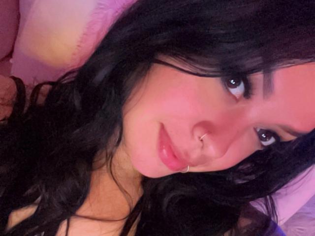 A vulva de MaveParker está centralizada, com as pernas abertas, mostrando uma pequena área de pelos pubianos. Ela tem tatuagens na barriga, um piercing no umbigo e unhas longas e brancas. Vela abaixo..