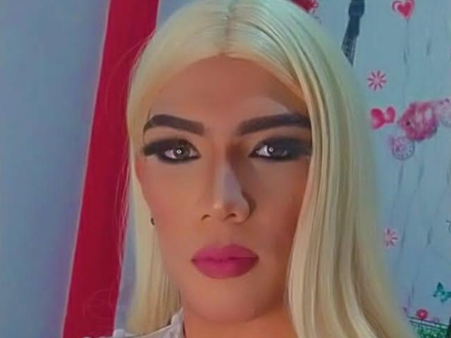 RoxanaLatinaTrans has blonde hair, heavy black eyeliner, thick eyebrows, and pink lipstick. Her eyes are dark and she's looking straight at the camera with a serious expression.