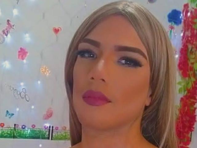 RoxanaLatinaTrans has blonde hair, blue eyes, and pink lipstick. She's looking at the camera with a slight smile, showing off her makeup and full, round ass.