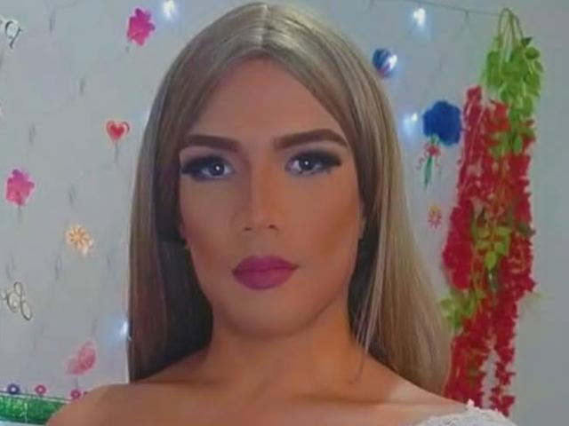 RoxanaLatinaTrans has long blonde hair, blue eyes, and pink lipstick. She's looking straight at the camera with a serious expression. Her tits are partially visible.