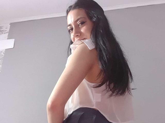 SerenaRin with long black hair, looking over her shoulder, wearing a sheer white top and black skirt, showing her bare ass. She has a cute, confident smile.