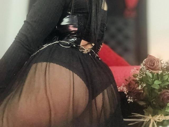 LombanaX's black sheer dress reveals her round ass, showing black lace-up underwear and a black leather corset with chains, her long black hair down.