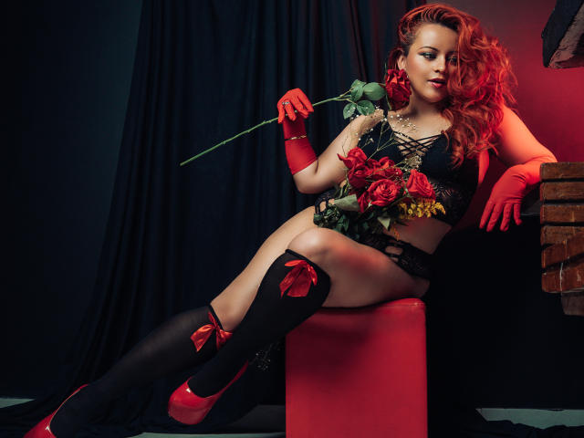 LillyBigAss with red roses, black lace lingerie, red gloves, black thigh-highs, and red heels, holding a rose, sitting on a red cube, sexy and confident.