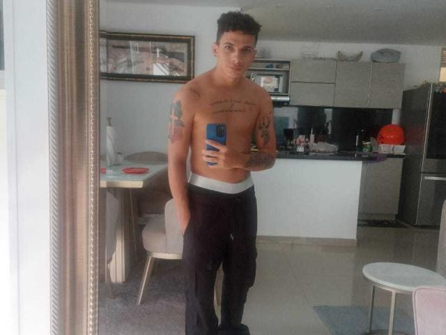 HottLoverGuy69, shirtless with tattoos, holding phone, wearing black pants, standing in front of mirror, showing a clean, muscular, attractive, brown-skinned, curly-haired, sexy body.