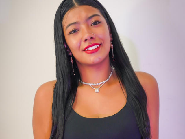 Ailyn Campos, met lang zwart haar, rode lippenstift, een neusring en een zilveren ketting, draagt een zwarte tanktop, glimlacht met rode lippen en heeft een glanzende neus..